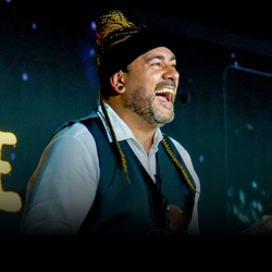 Imagem de Rcky Chaves olhando para o palco com uma expressão alegre.